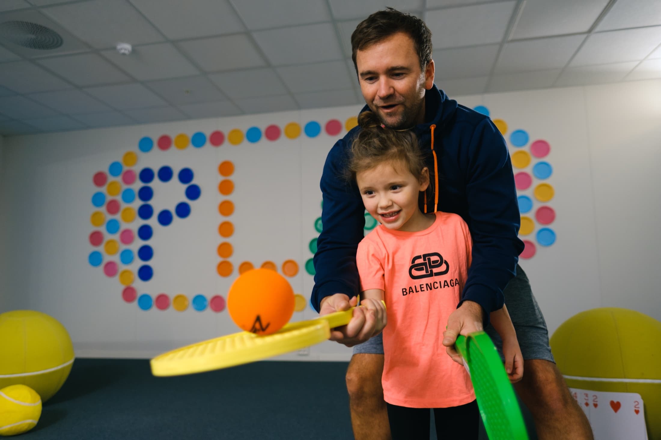 En trener hjelper en liten jente med tennisracketen