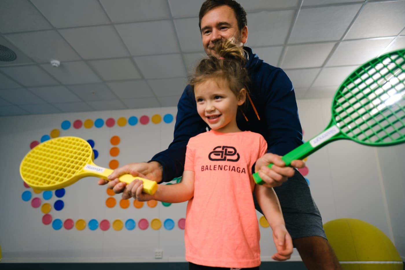 Far og datter leker tennis med fargerike racketer innendørs